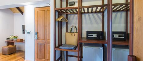 A compact room with a wooden shelving unit containing a handbag, a small refrigerator, and a hanging garment rack.
