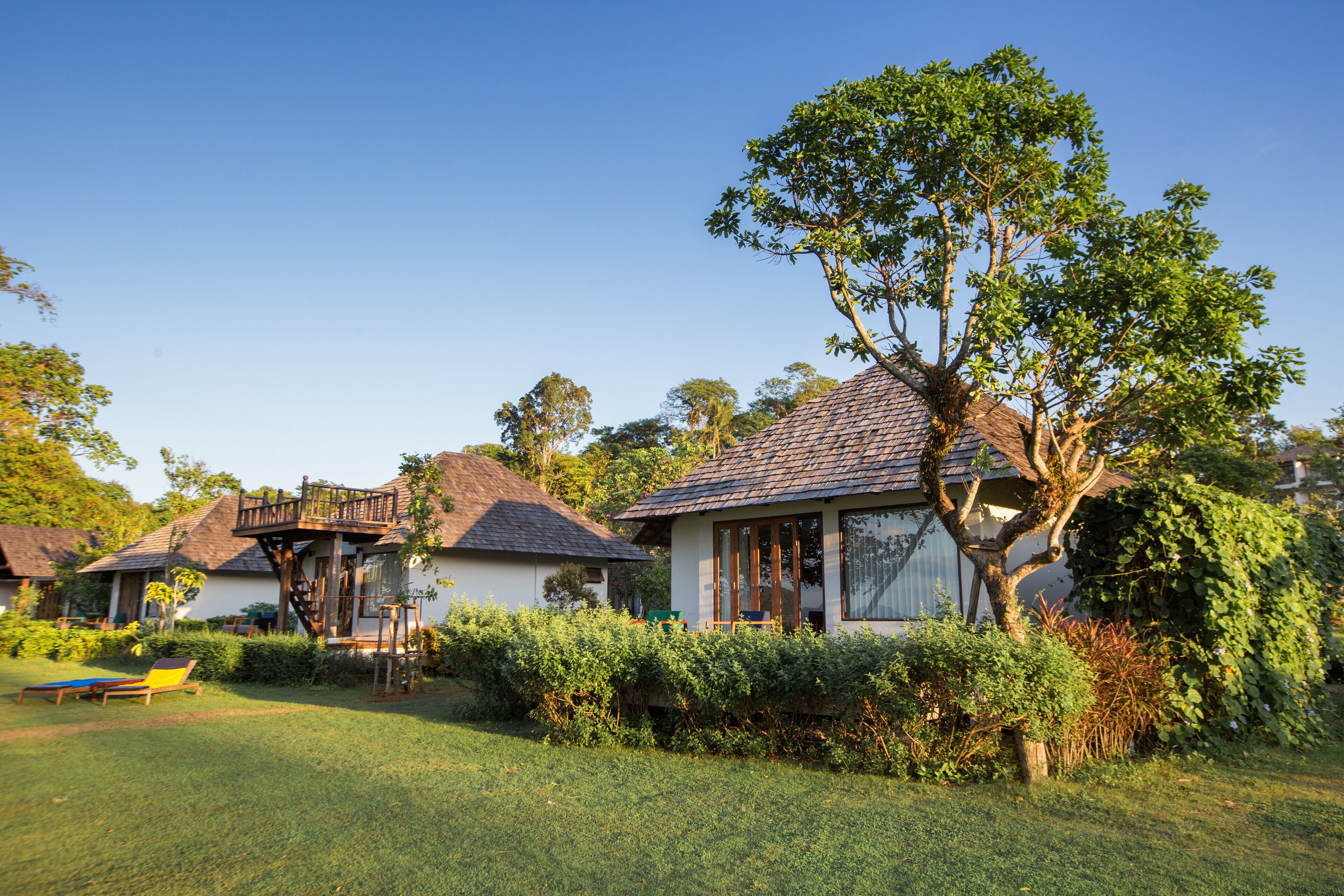Une maison de style bungalow, dotée d’un toit en tuiles, entourée d’une végétation luxuriante et d’une pelouse bien entretenue.