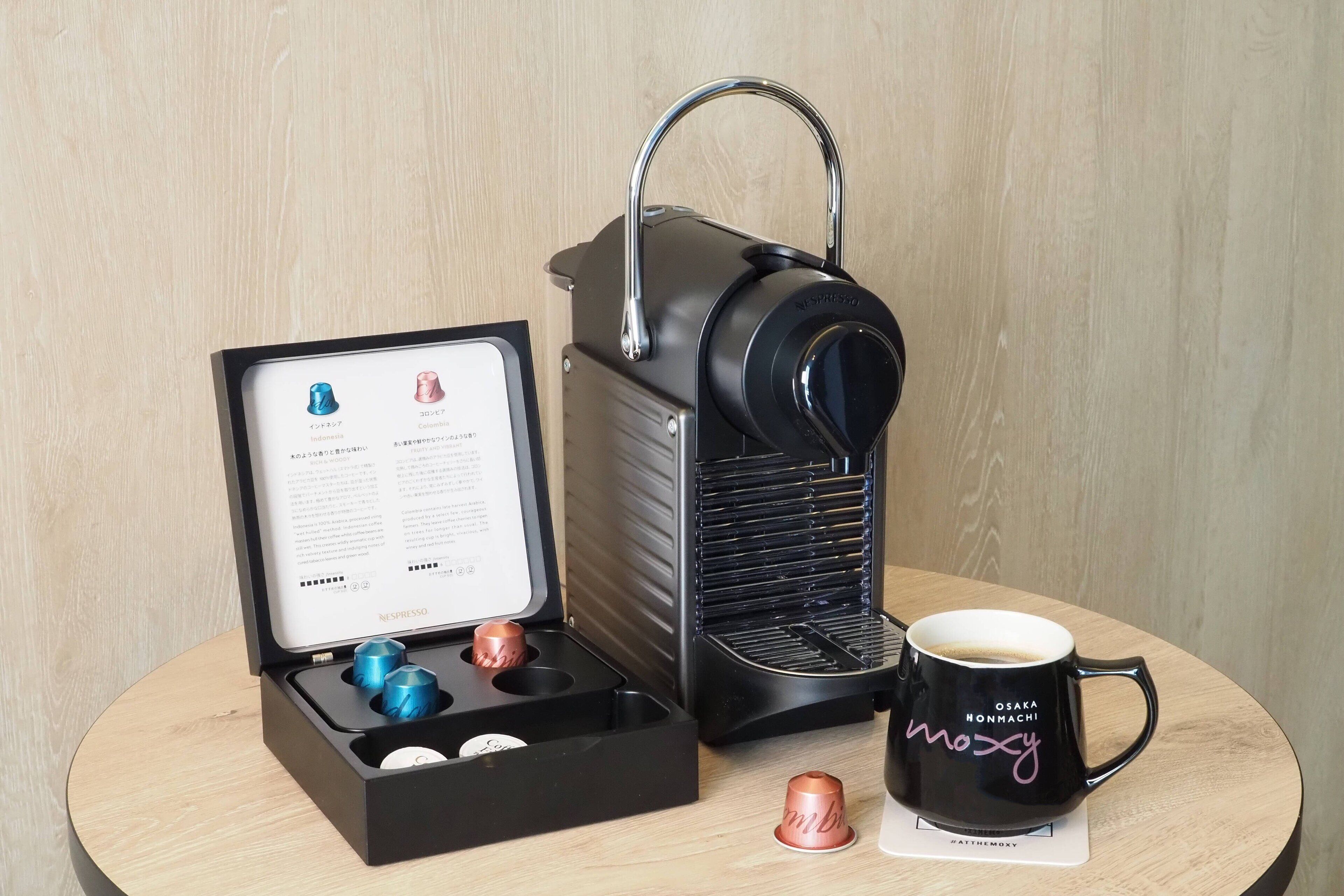 Una macchina da caffè con una caffettiera manuale, una tazza di caffè e una confezione di capsule di caffè.