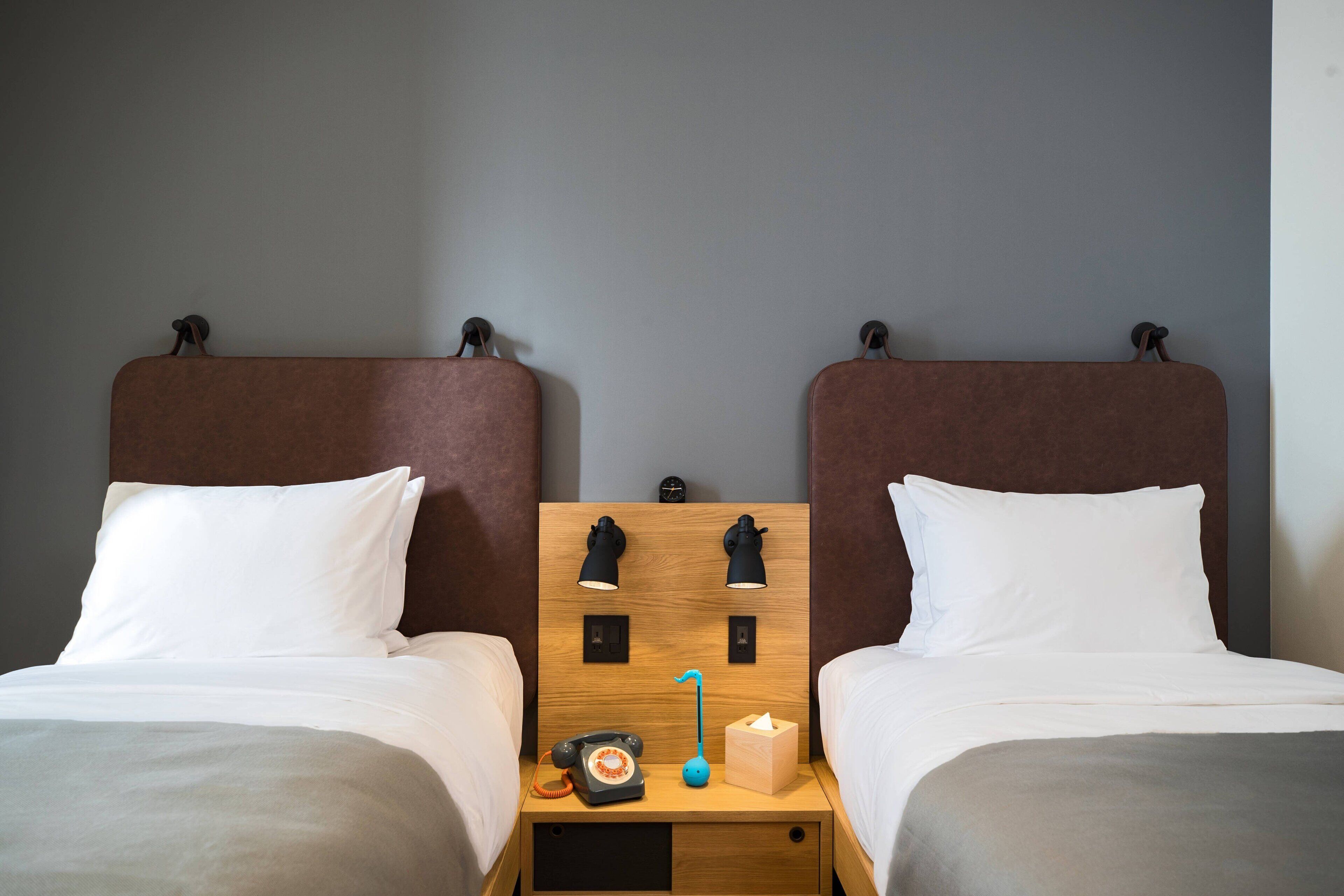 A hotel room with two single beds, a wooden headboard, bedside lamps, a telephone, a tissue box, and a small drawer.