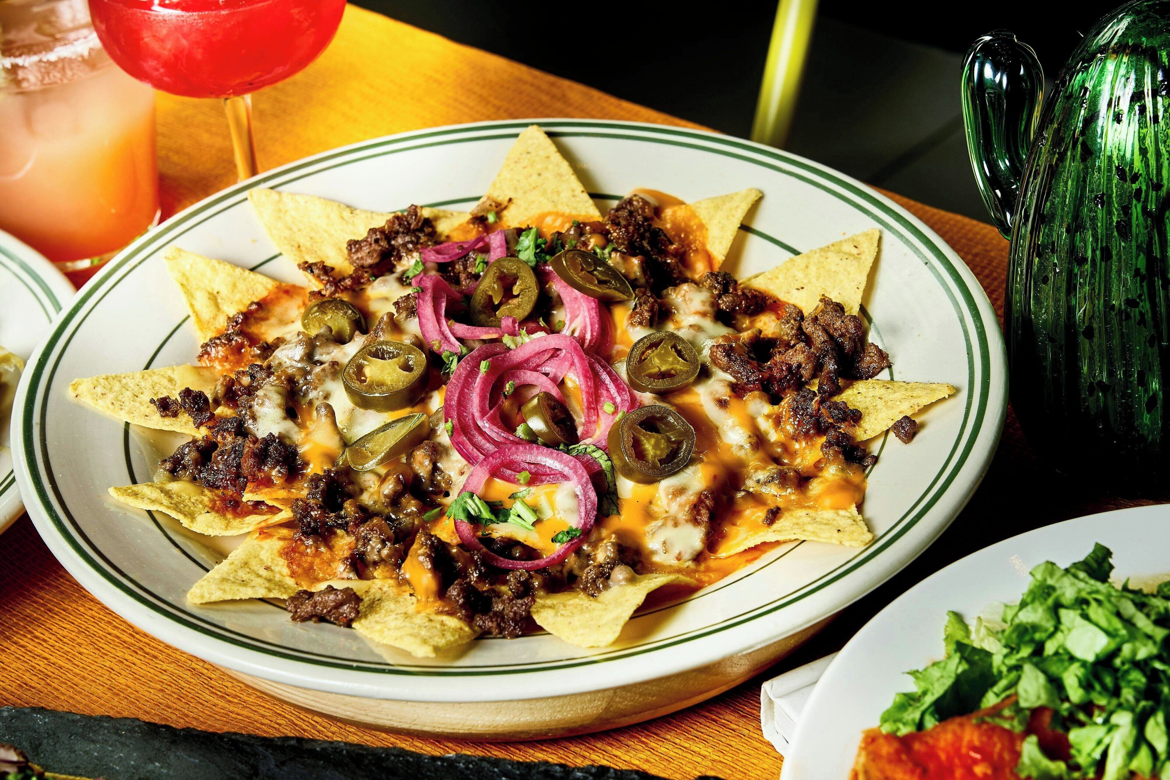 A plate of nachos topped with meat, cheese, jalapeños, and red onions.
