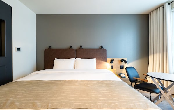 A hotel room with a large bed, a desk, a chair, and a lamp.