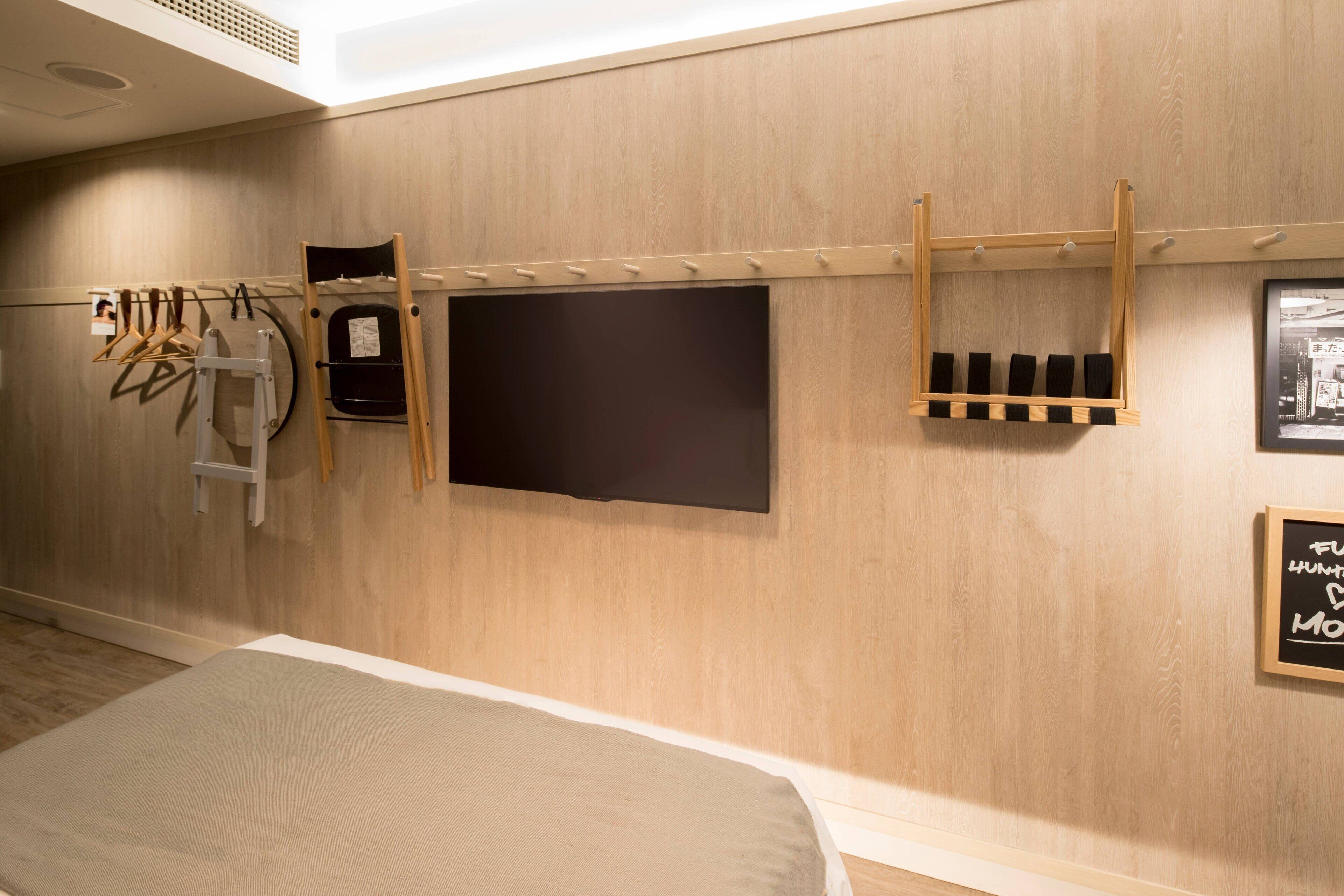 Hotelkamer met een bed, een wandtelevisie, een kapstok en een houten plank met flessen.