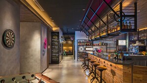 Un área de bar con taburetes, un dardo y una mesa de fútbolín.