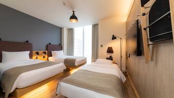 Habitación de hotel con dos camas, suelo de madera, una luz en el techo y un televisor fijado a la pared.