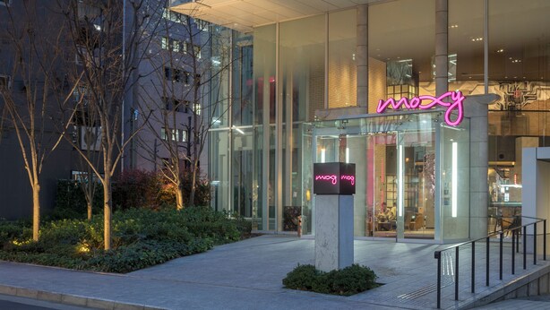 Un edificio moderno con fachada de vidrio y un letrero de neón que dice "mozy".