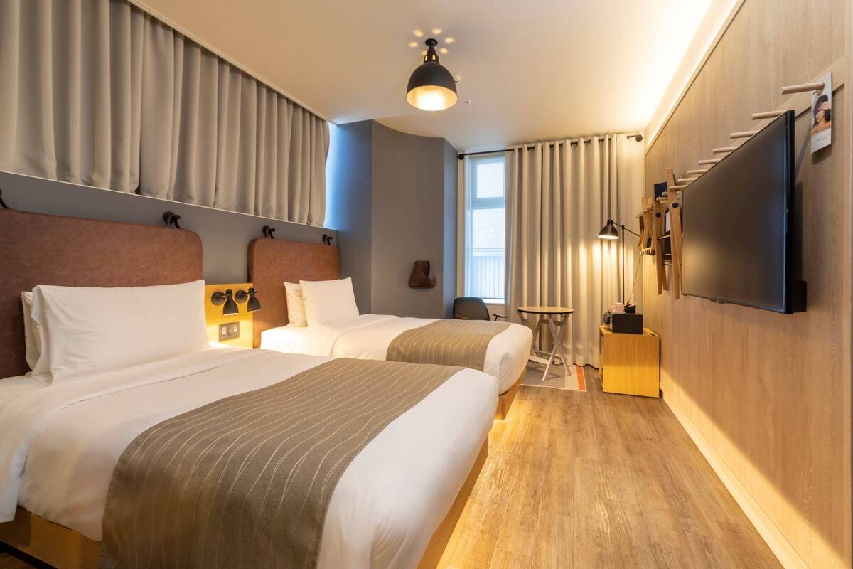 Une chambre d’hôtel avec deux lits, un téléviseur à écran plat, une petite table et une lampe.