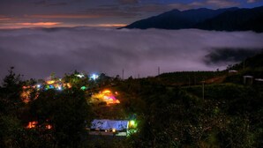 A night view of a mountainous area with a village below, featuring illuminated buildings and a blanket of clouds between the village and the mountains. - AiShangXiWeng B&B (Wufeng)