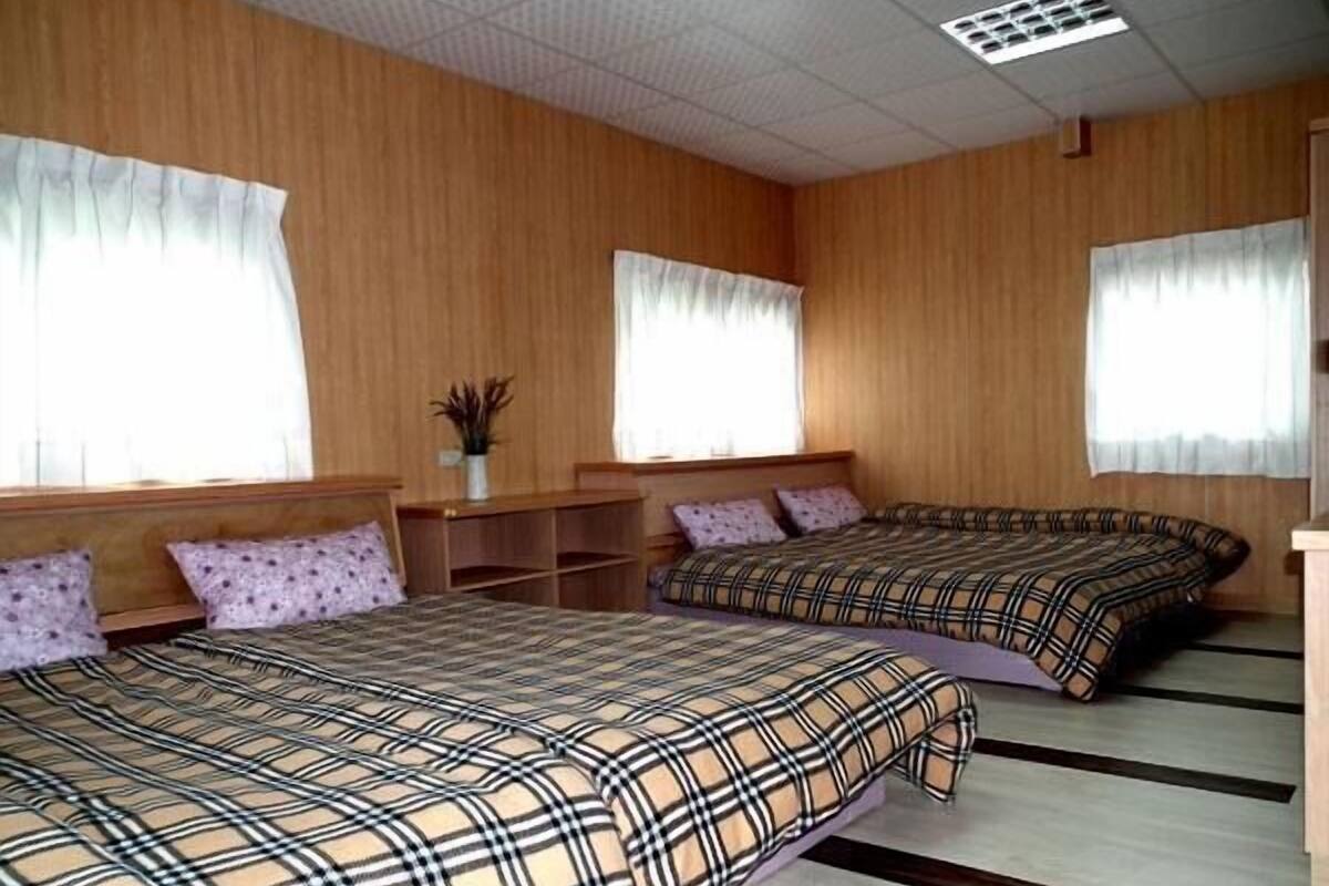 A room with two beds, wooden walls, and a window with curtains.