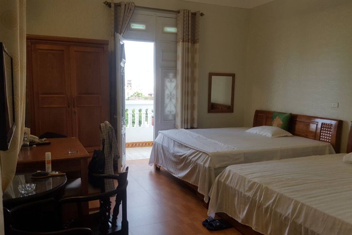 A hotel room with two beds, a desk, a chair, a TV, and a balcony.