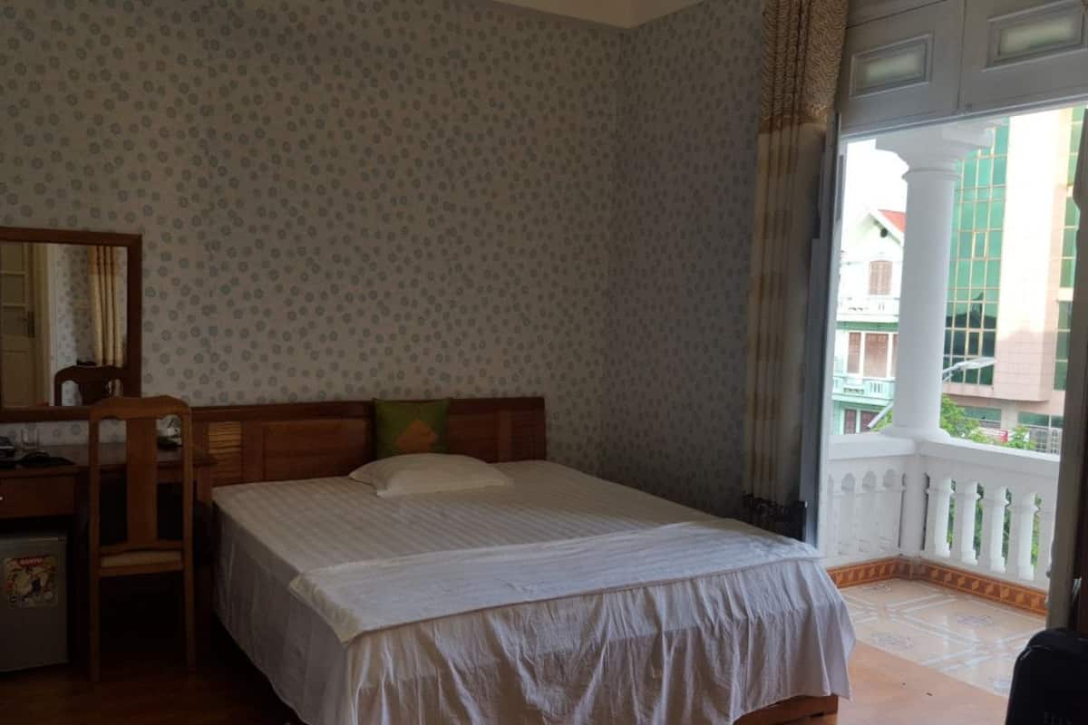 A bedroom with a bed, a desk, a chair, a mirror, and a balcony with a railing.