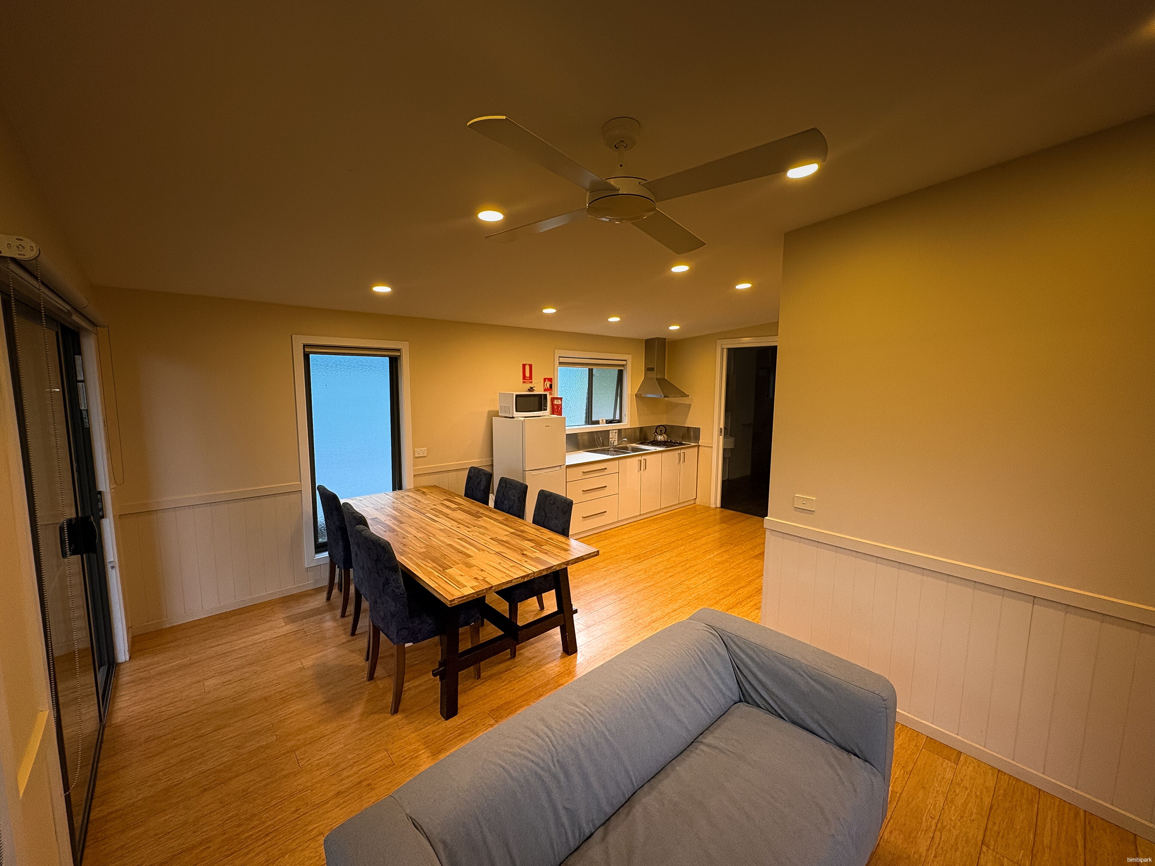 A modern kitchen with a dining area, a ceiling fan, and a large window.