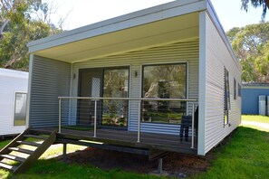 A single-story mobile home with a covered porch, large sliding glass doors, and a small outdoor seating area.