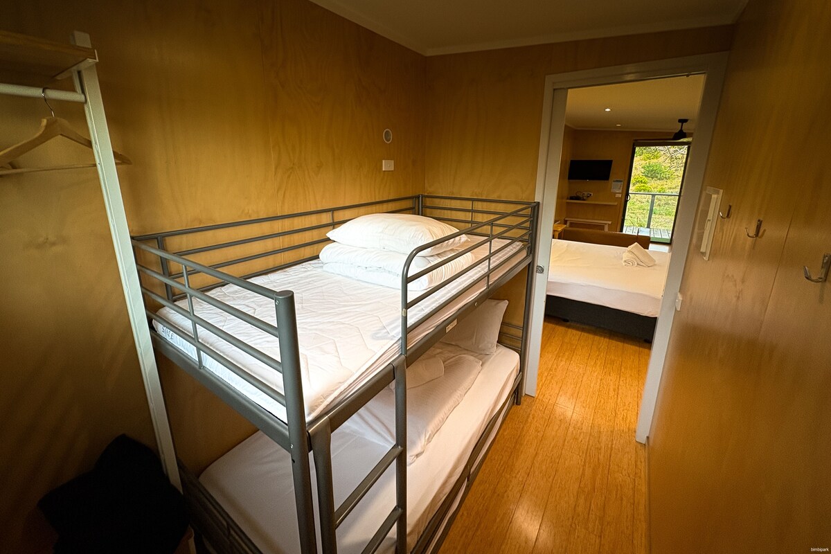 Une chambre avec des lits superposés, un plancher en bois et une porte donnant sur une autre pièce.