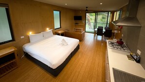 Habitación de hotel moderna con una cama grande, un escritorio pequeño, una kitchenette y un ventanal corredero al exterior.