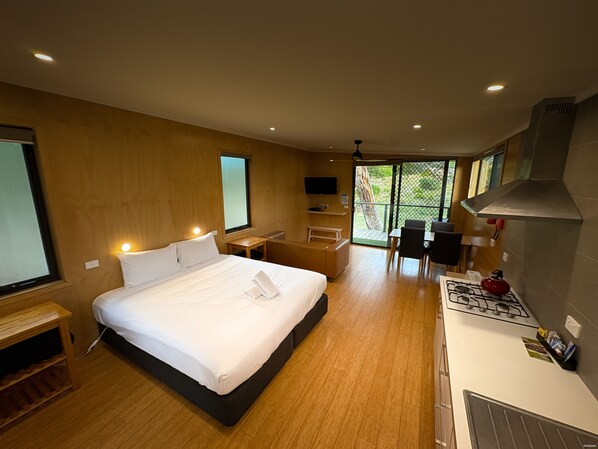 Une chambre d’hôtel moderne dotée d’un grand lit, d’un petit bureau, d’une kitchenette et d’une porte-fenêtre coulissante donnant sur l’extérieur.