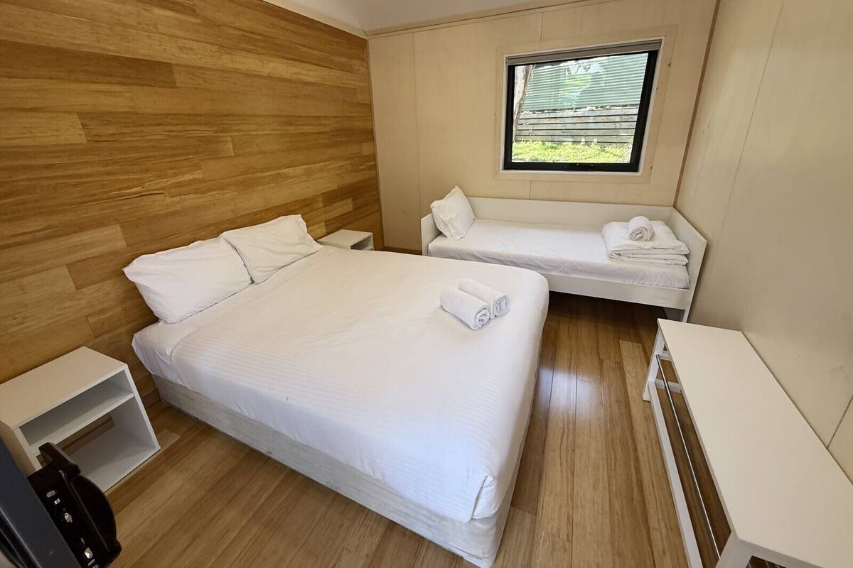 A hotel room with a large bed, two smaller beds, a window with blinds, and a wooden wall.