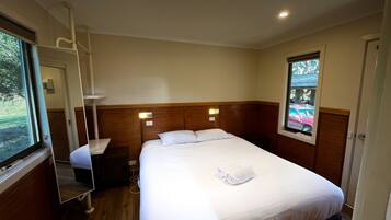 Quarto de hotel com uma cama de solteiro, mesa de cabeceira, espelho, janela com vista para o exterior e cabeceira de madeira.