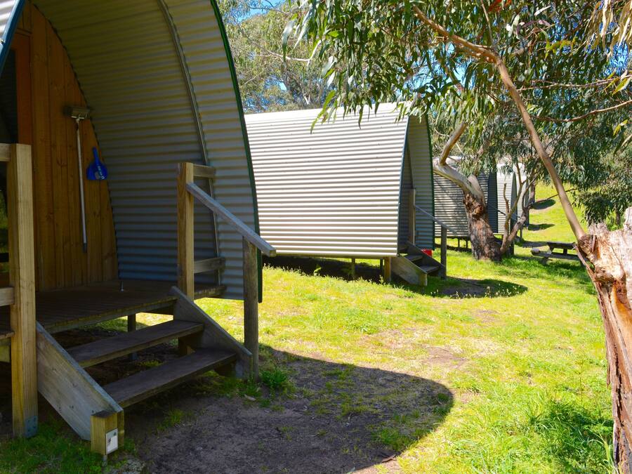 A series of small, single-story cabins with wooden steps leading to the entrance, surrounded by grass and trees.