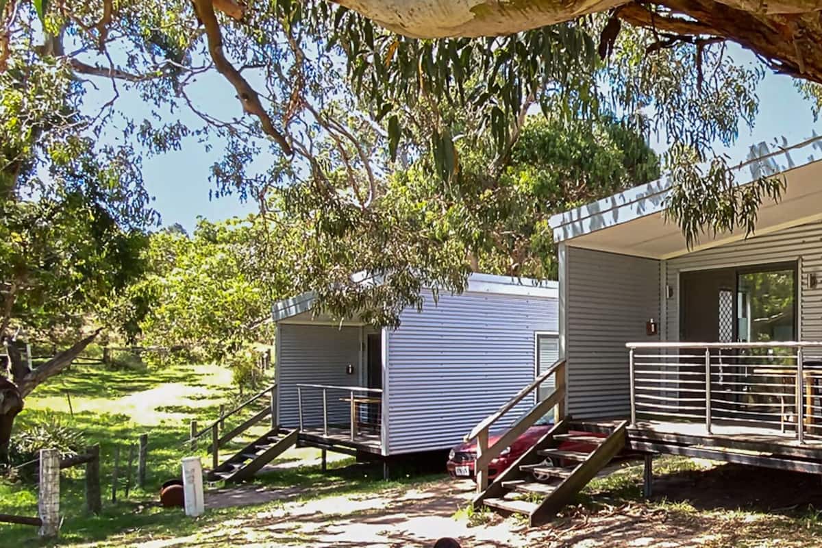 Two mobile homes with external staircases, surrounded by trees and a grassy area.