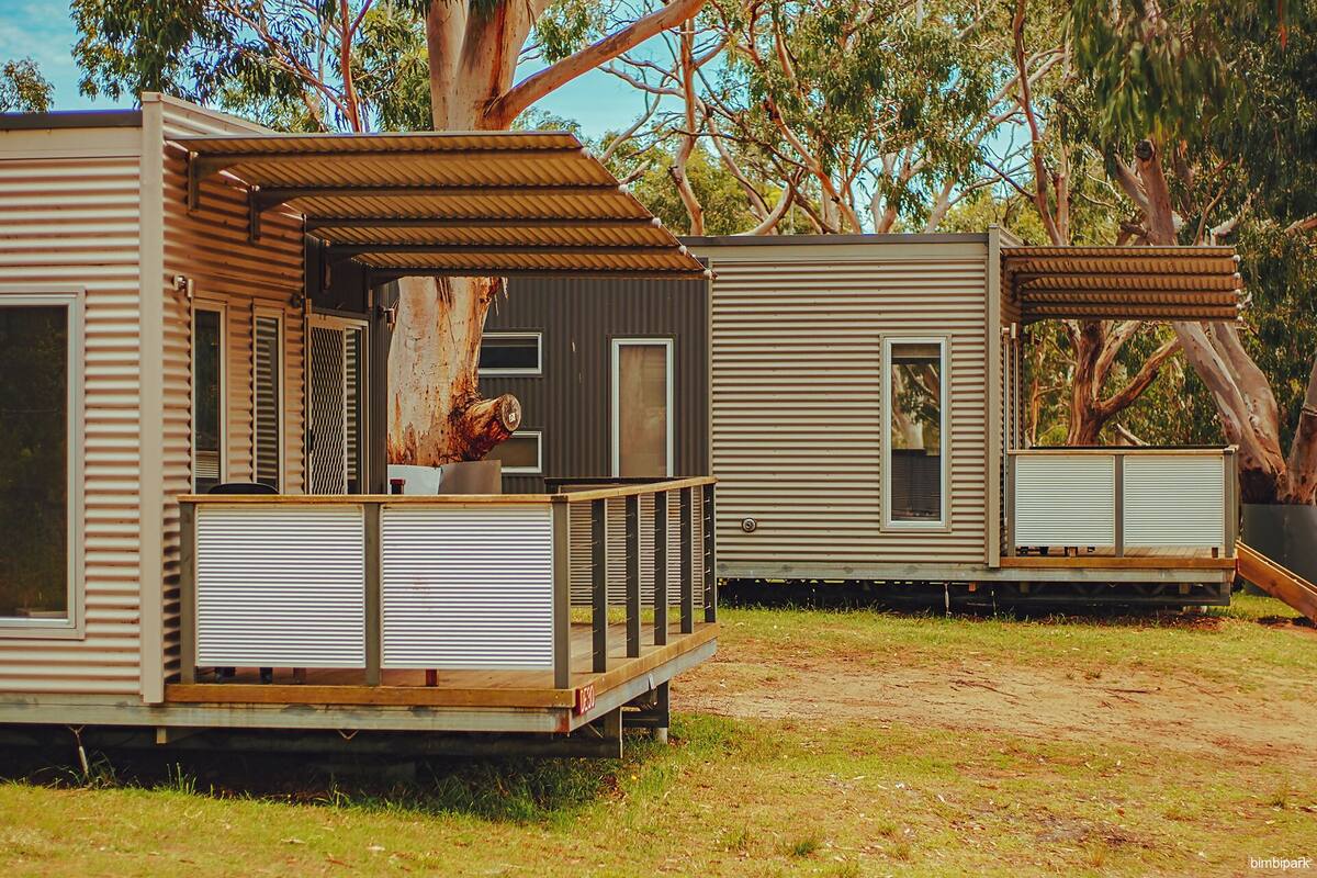 Two mobile homes with metal siding, wooden decks, and large windows.