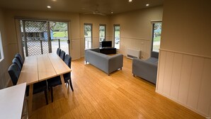 Una habitación amplia con suelo de madera, una mesa de comedor con sillas, un sofá gris, un televisor y un ventilador de techo.