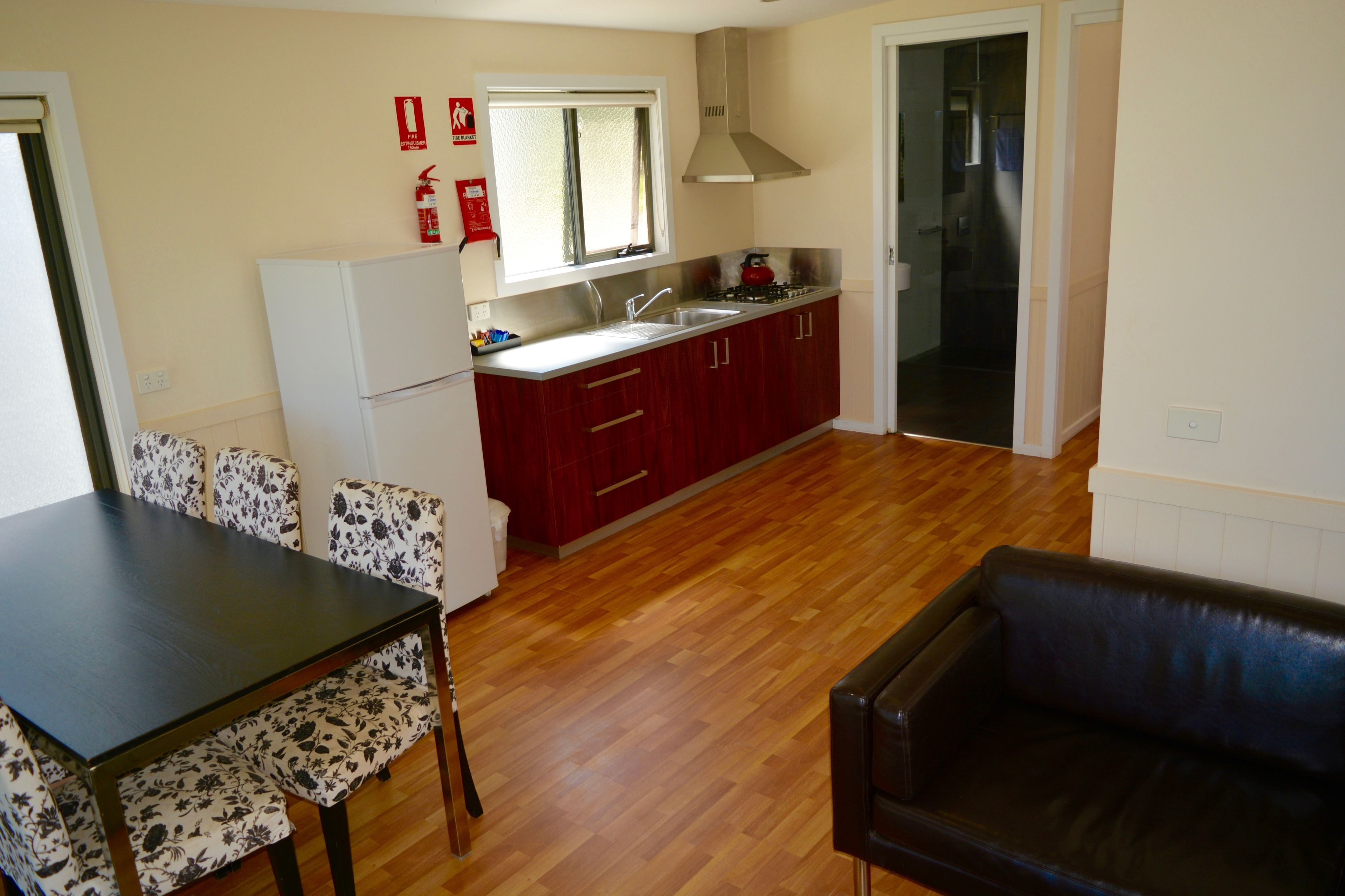 Cocina compacta con piso de madera, comedor con sillas de estampado floral y un sofá de cuero negro.