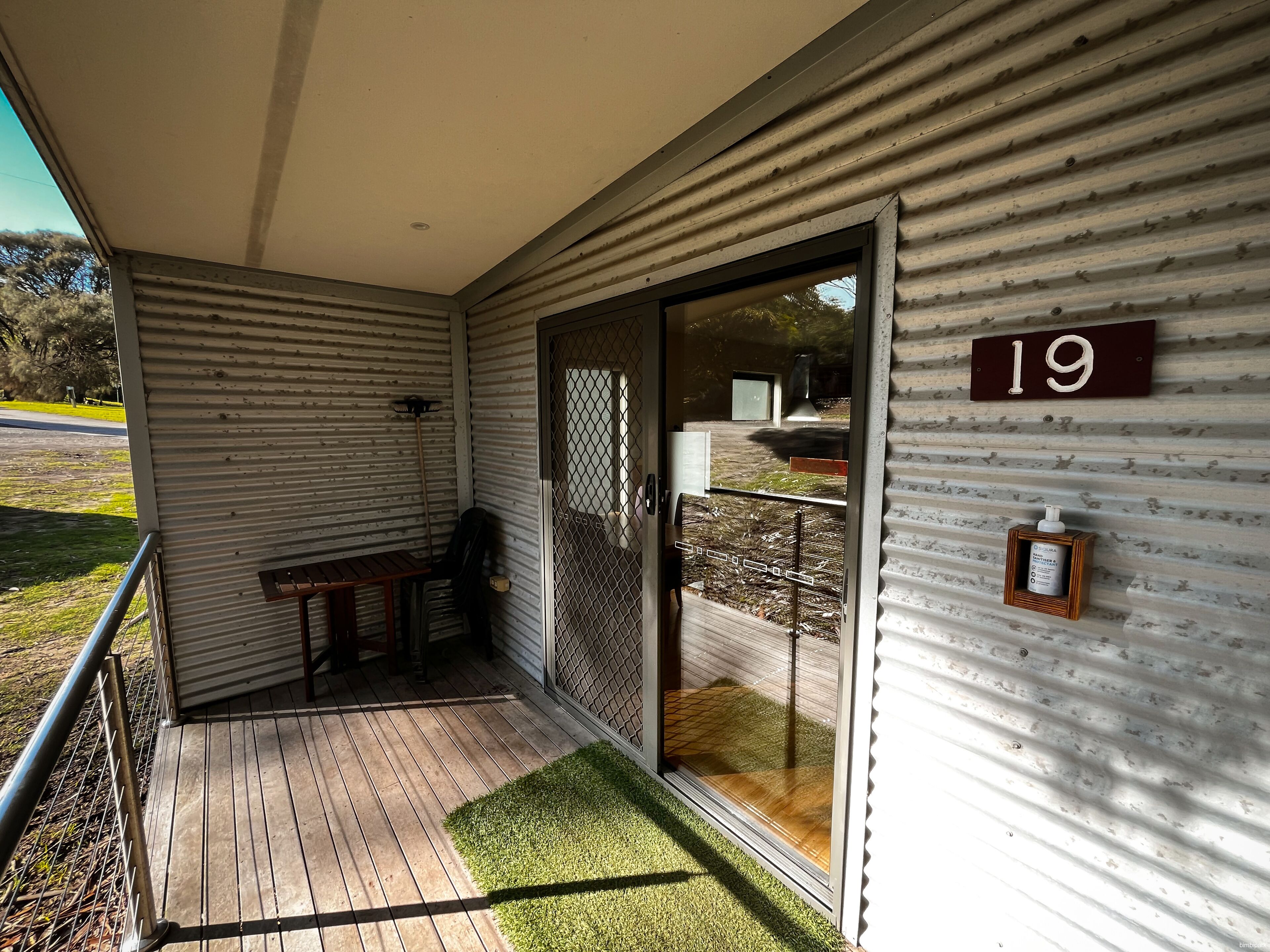 A covered porch with a wooden bench, a metal railing, and a number '19' sign on the wall.