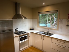 Une cuisine moderne avec des armoires blanches, une hotte de cuisinière en acier inoxydable, une cuisinière à gaz, un four à micro-ondes encastré et une fenêtre donnant sur les arbres.