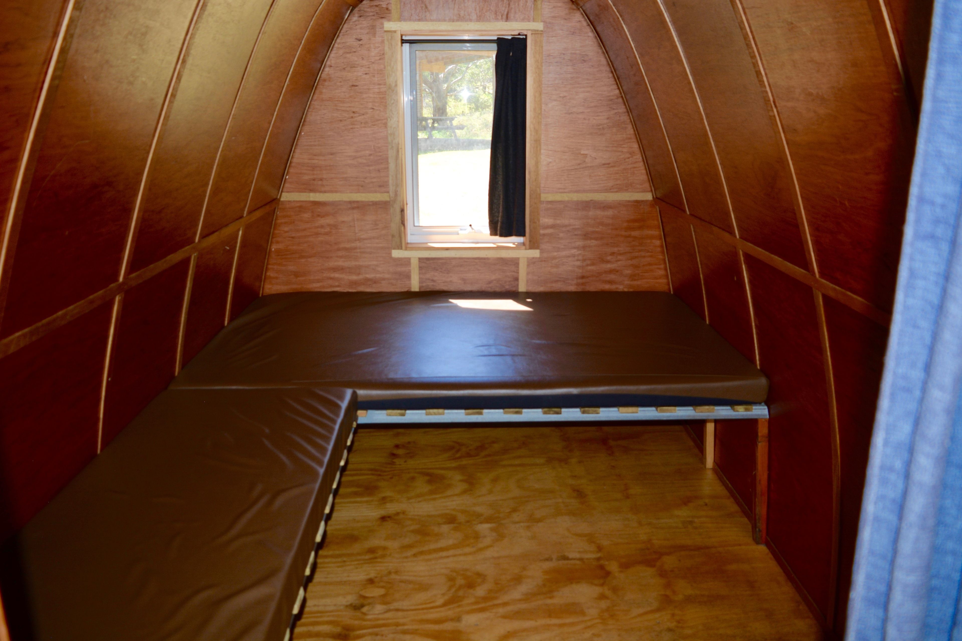 Een kleine, driekantige zolderkamer met een enkel bed, een raam en houten wanden.