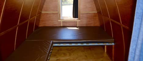 Een kleine, driekantige zolderkamer met een enkel bed, een raam en houten wanden.