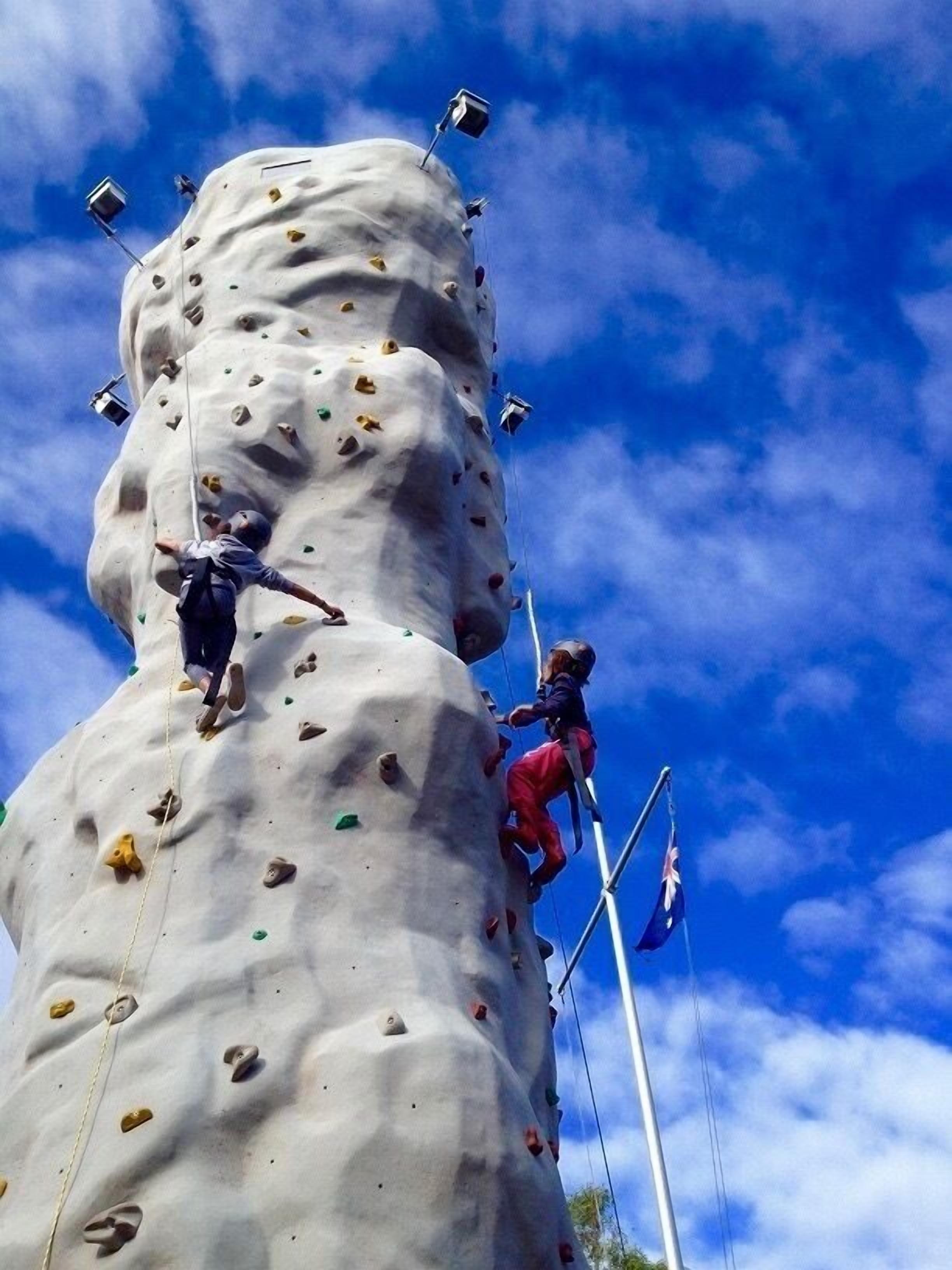 A large rock climbing wall with various holds and a climber in mid-climb.