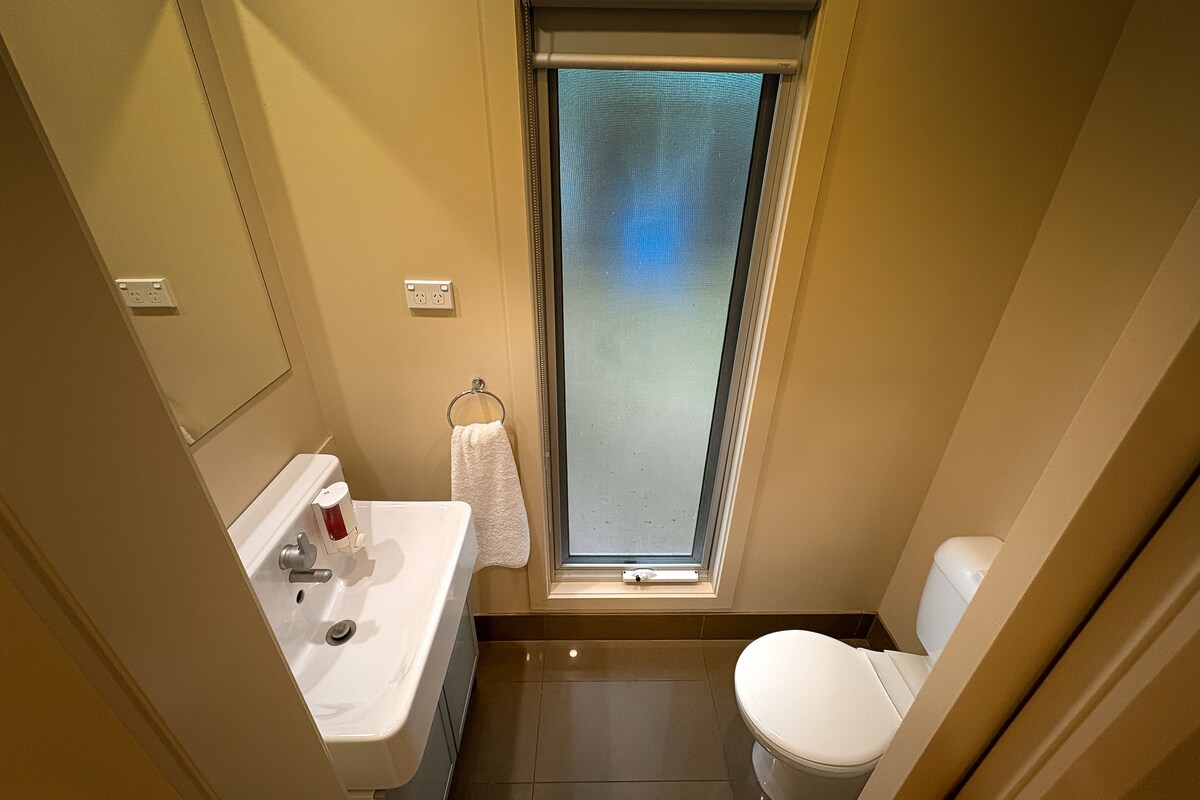 Une petite salle de bain avec un lavabo blanc, des toilettes et une fenêtre avec un vitrage dépoli.