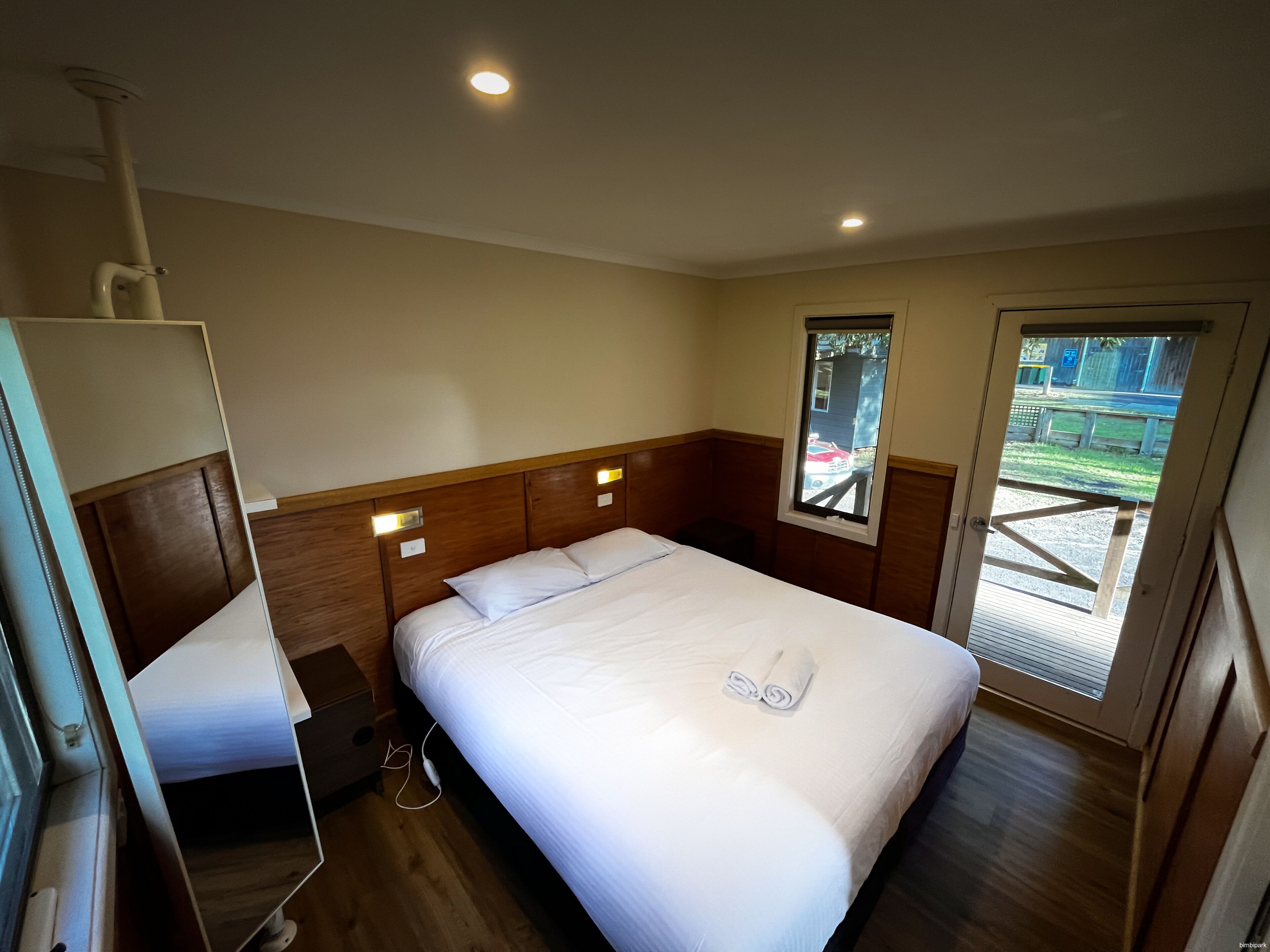 A hotel room with a bed, bedside table, and a window with a view of the outside.