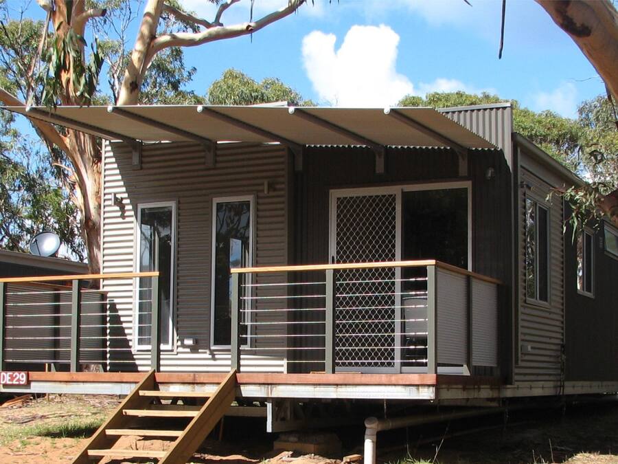 Une maison mobile dotée d’une terrasse en bois, d’une rambarde en métal et d’un escalier menant à l’entrée.