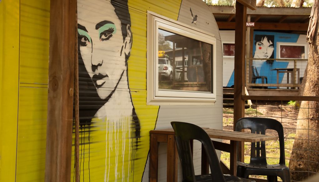 Un mural colorido sobre una pared amarilla, una ventana y una mesa con sillas.
