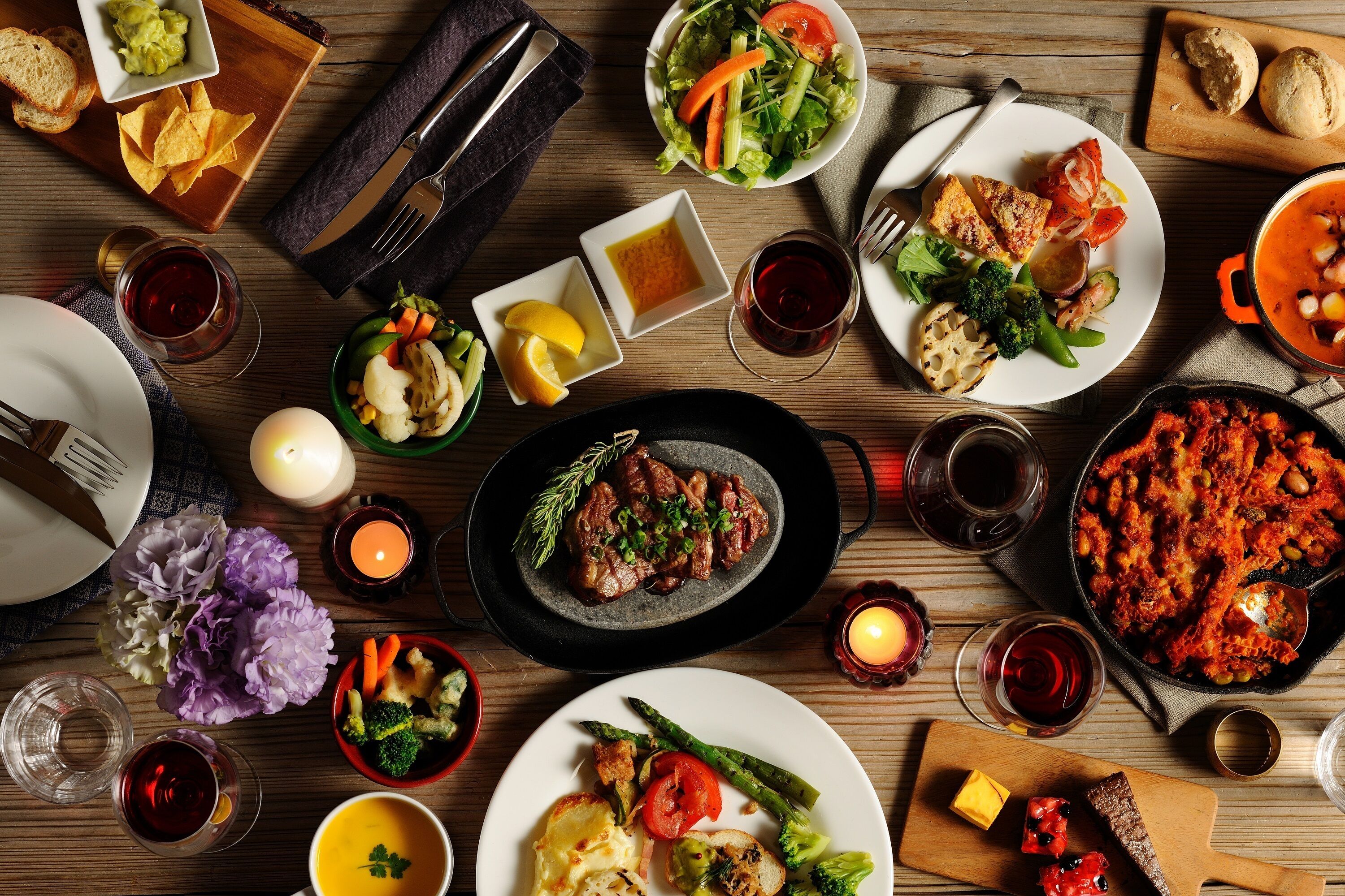 Mesa de comedor dispuesta con platos, bebidas y velas, que sugiere un montaje para una comida.