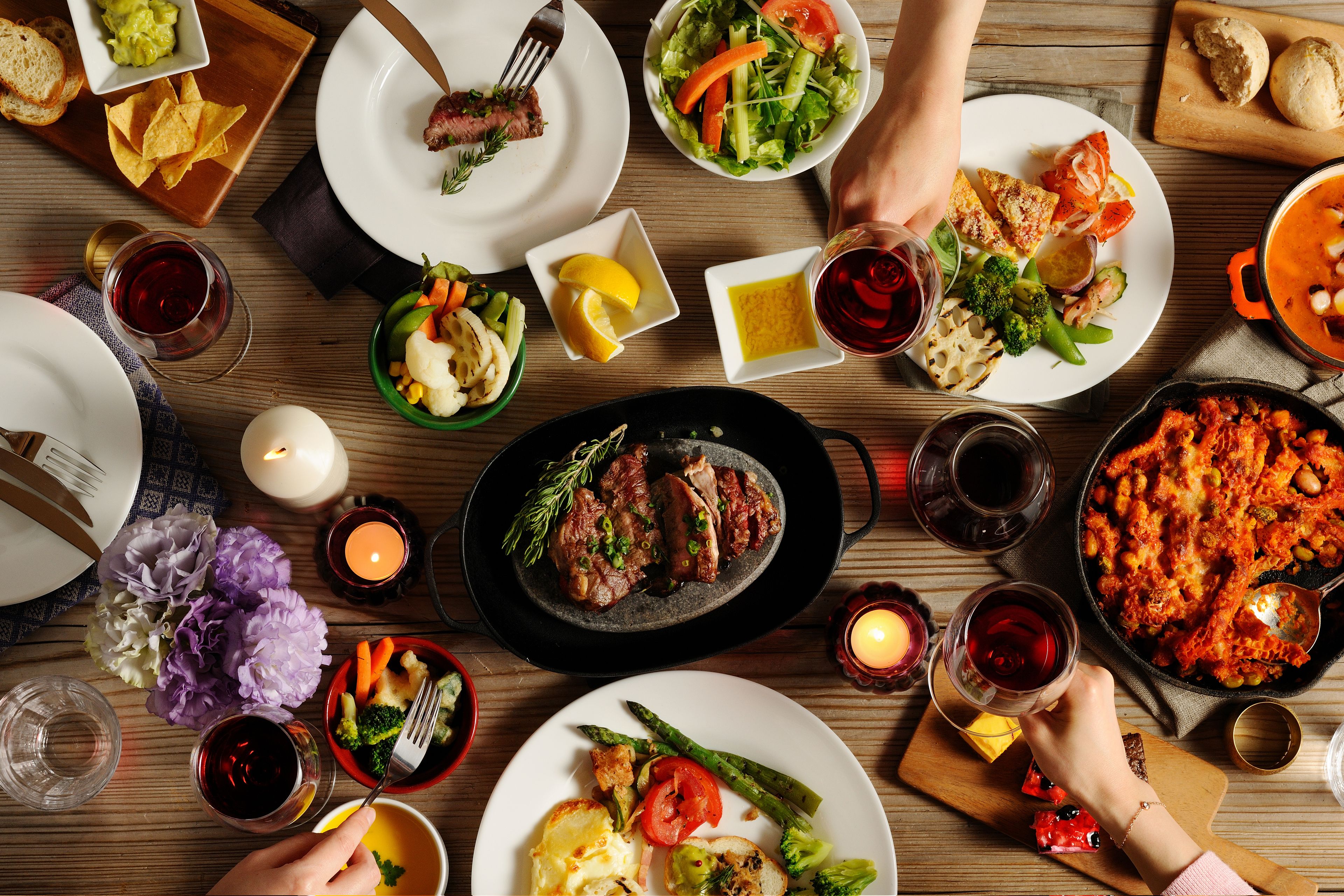 A dining table with various dishes, including steak, vegetables, and a pot of stew.
