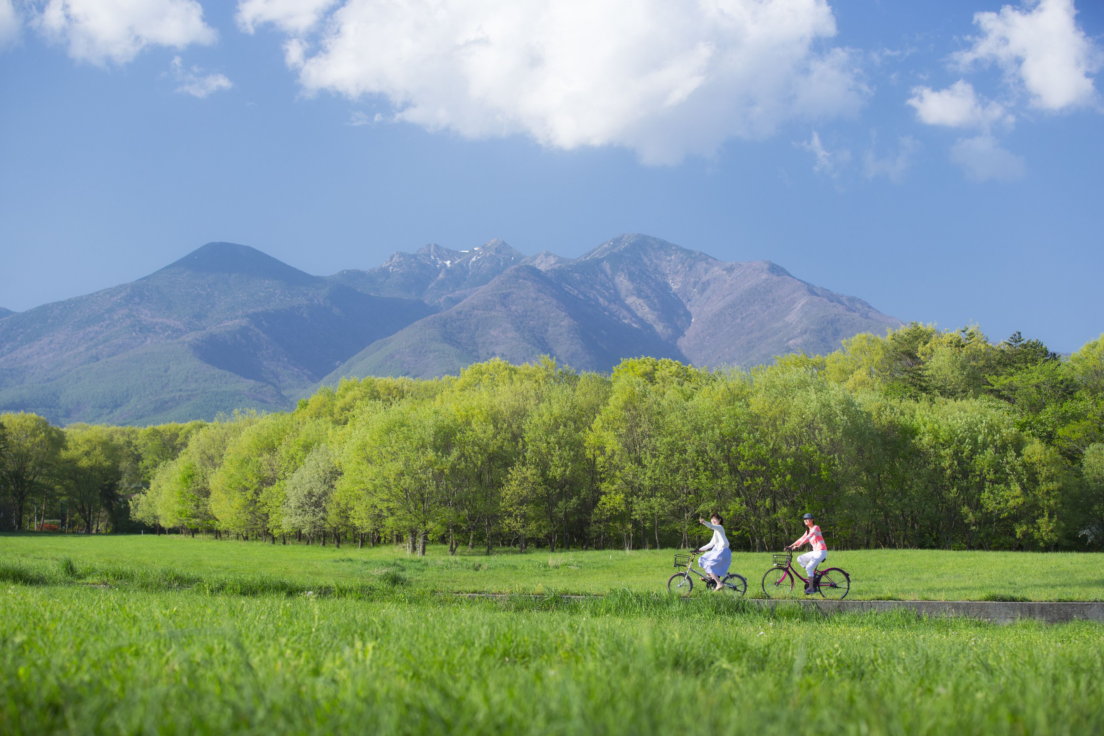 A field with two cyclists, a mountain range in the background, and a clear sky.