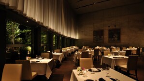 A dimly lit restaurant with tables set for dining, large windows, and a view of greenery outside. - Hoshino Resorts RISONARE Yatsugatake (Hokuto)