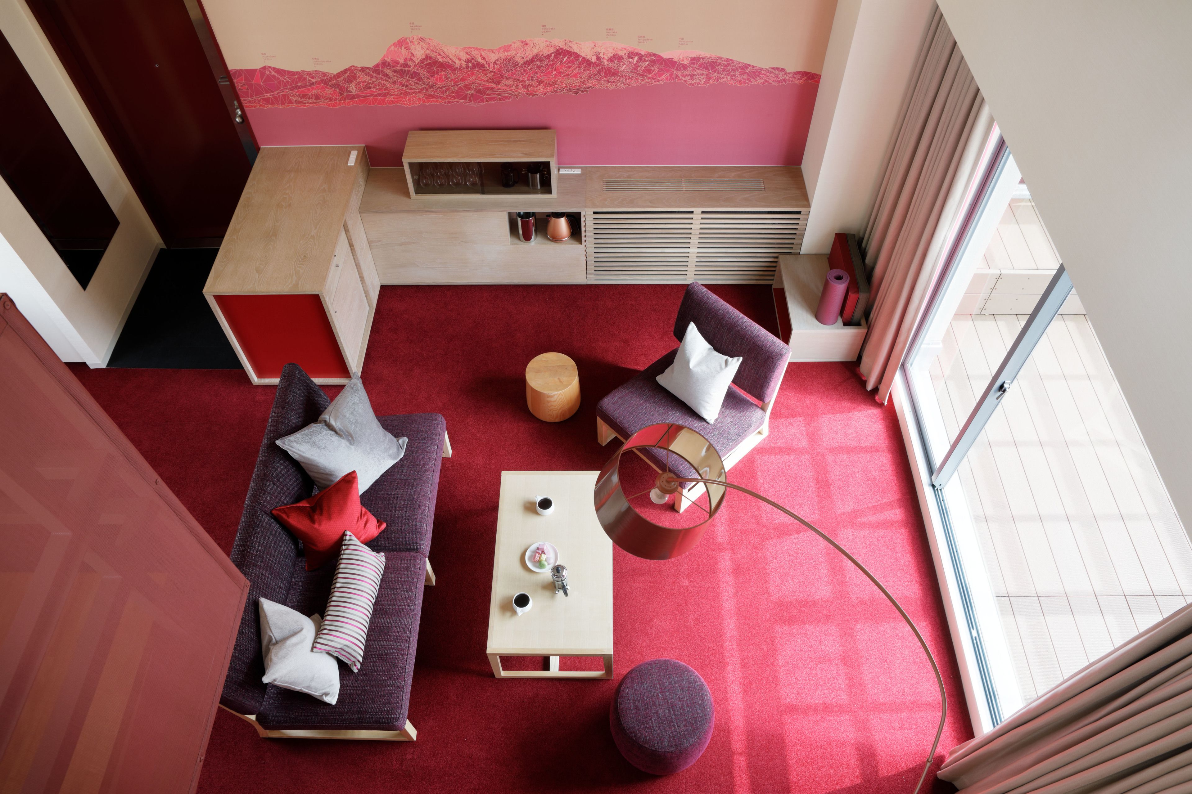 Una habitación de hotel moderna con alfombra roja, dos sofás, una mesita y una ventana con cortinas.