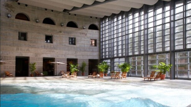 An indoor swimming pool with lounge chairs and potted plants, surrounded by stone walls and large windows. - Hoshino Resorts RISONARE Yatsugatake (Hokuto)