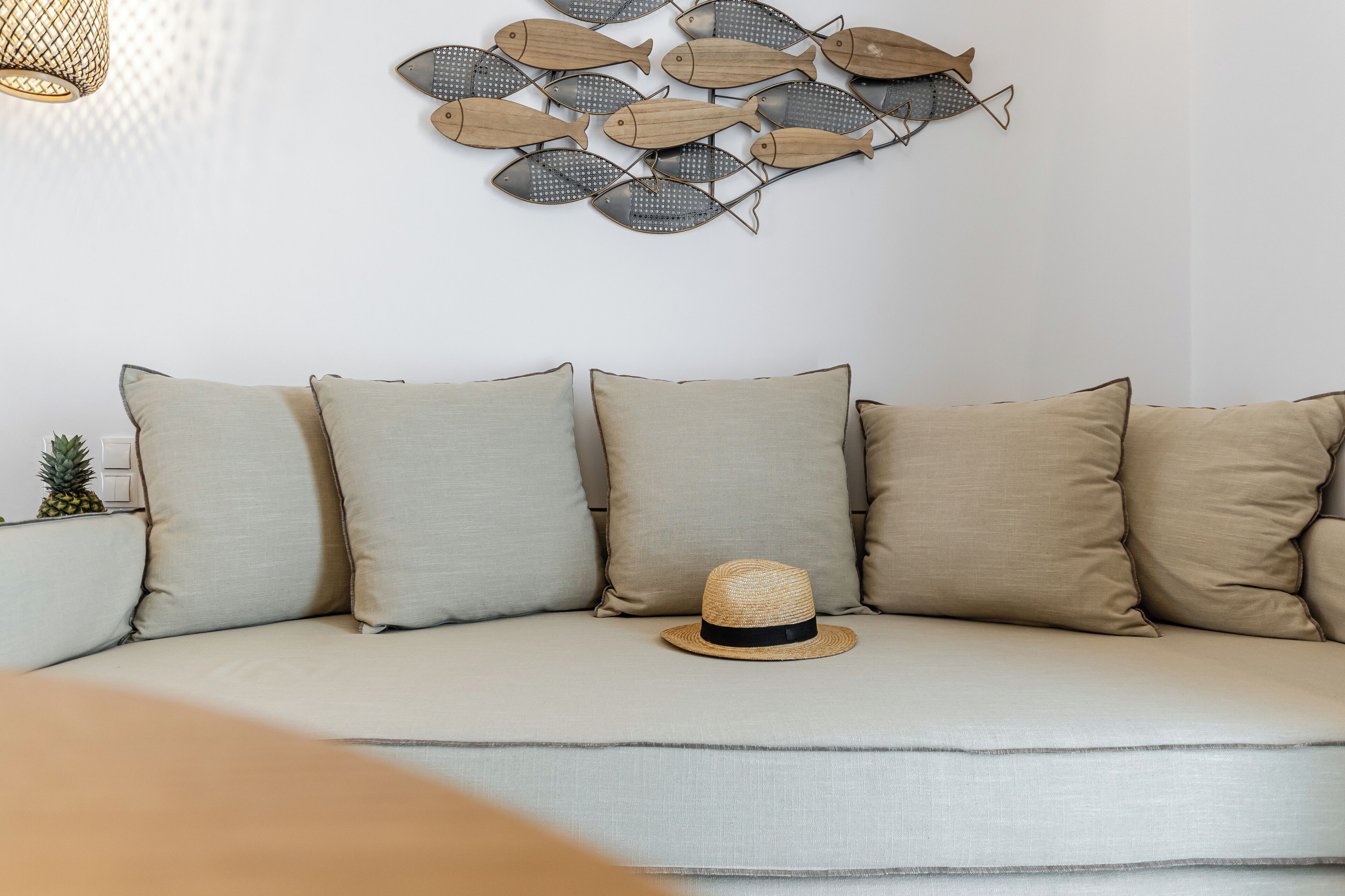 A sectional sofa with five cushions, a wall-mounted fish decoration, and a straw hat on the seat.