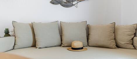 A sectional sofa with five cushions, a wall-mounted fish decoration, and a straw hat on the seat.