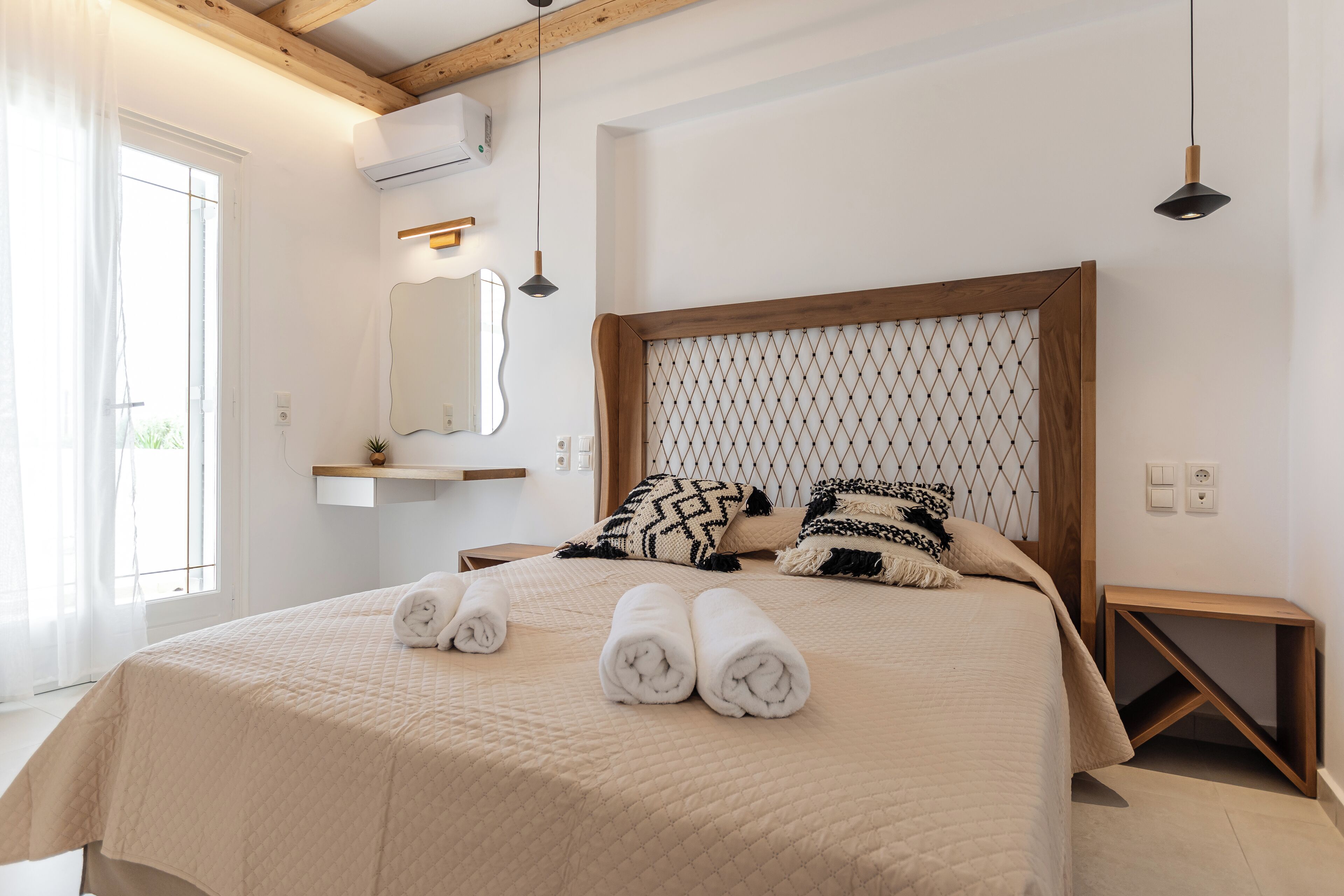 A neatly made bed with rolled towels, a wooden headboard, and a bedside table with a lamp.