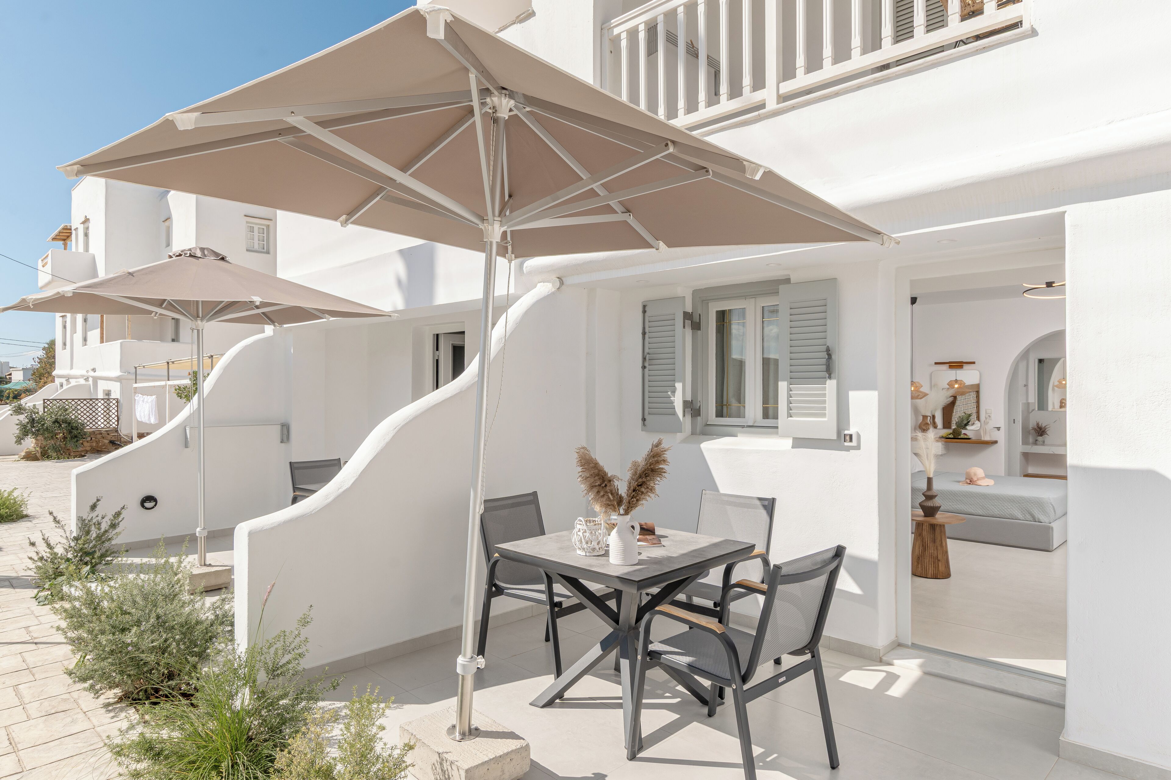 Een witte villa met een terras, compleet met een tafel, stoelen, een grote parasol en een trap naar de bovenverdieping.