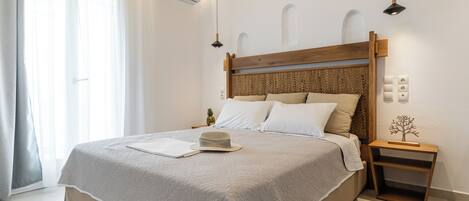 A neatly made bed with a wooden headboard, a bedside table with a lamp, and a small decorative tree.