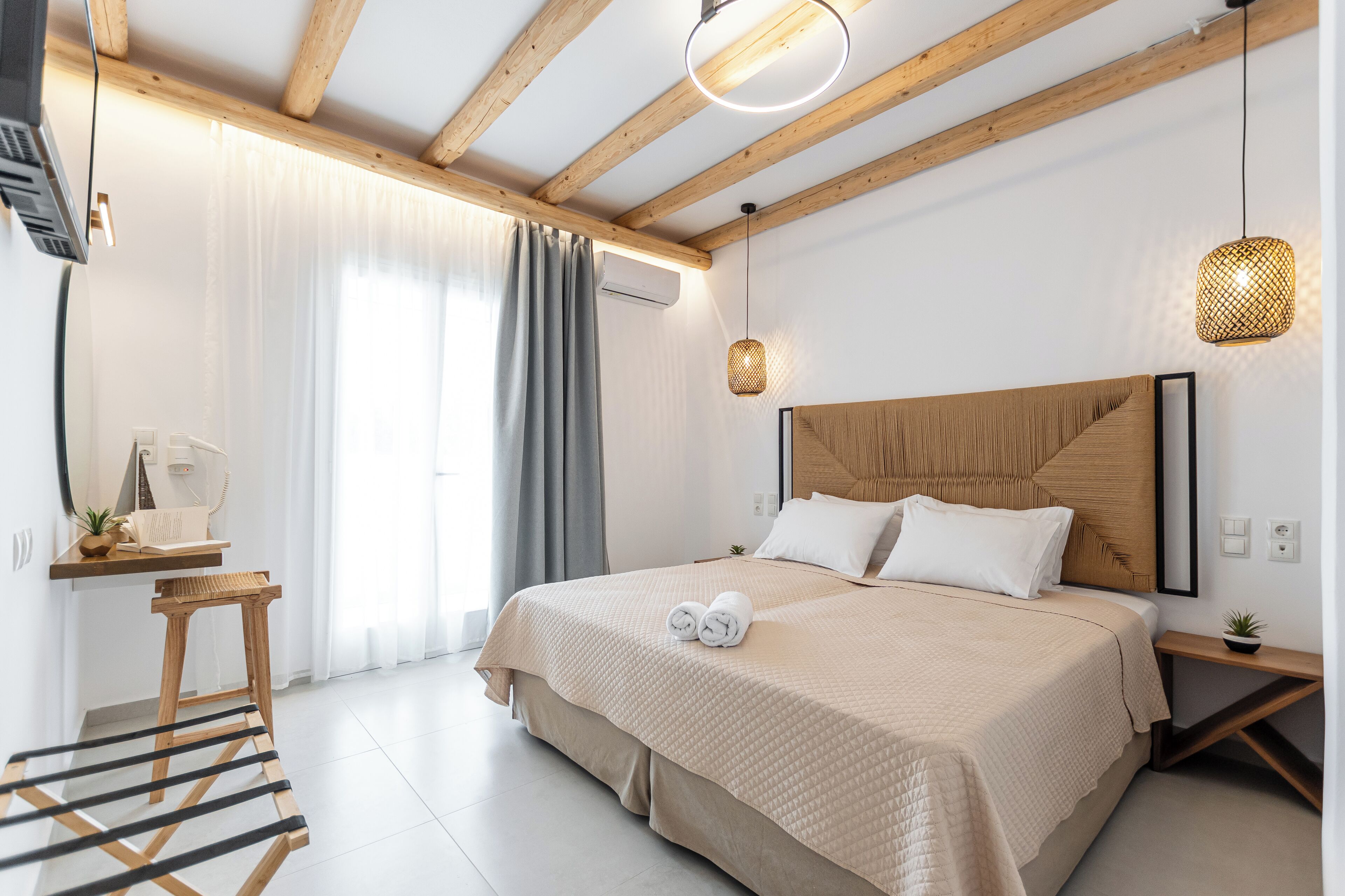 Un dormitorio moderno con una cama grande, vigas de madera, un escritorio con lámpara y un aplique.
