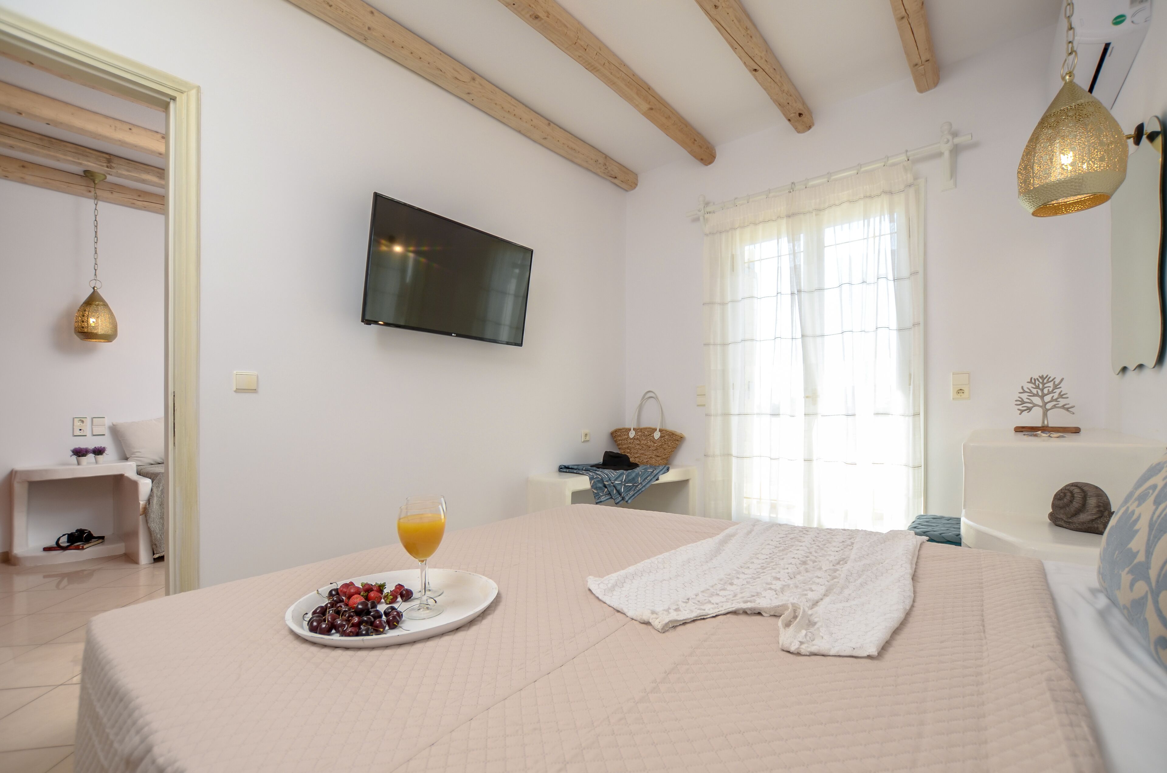 Un dormitorio con cama, televisión, ventana con cortinas y mesita de noche con cesta.