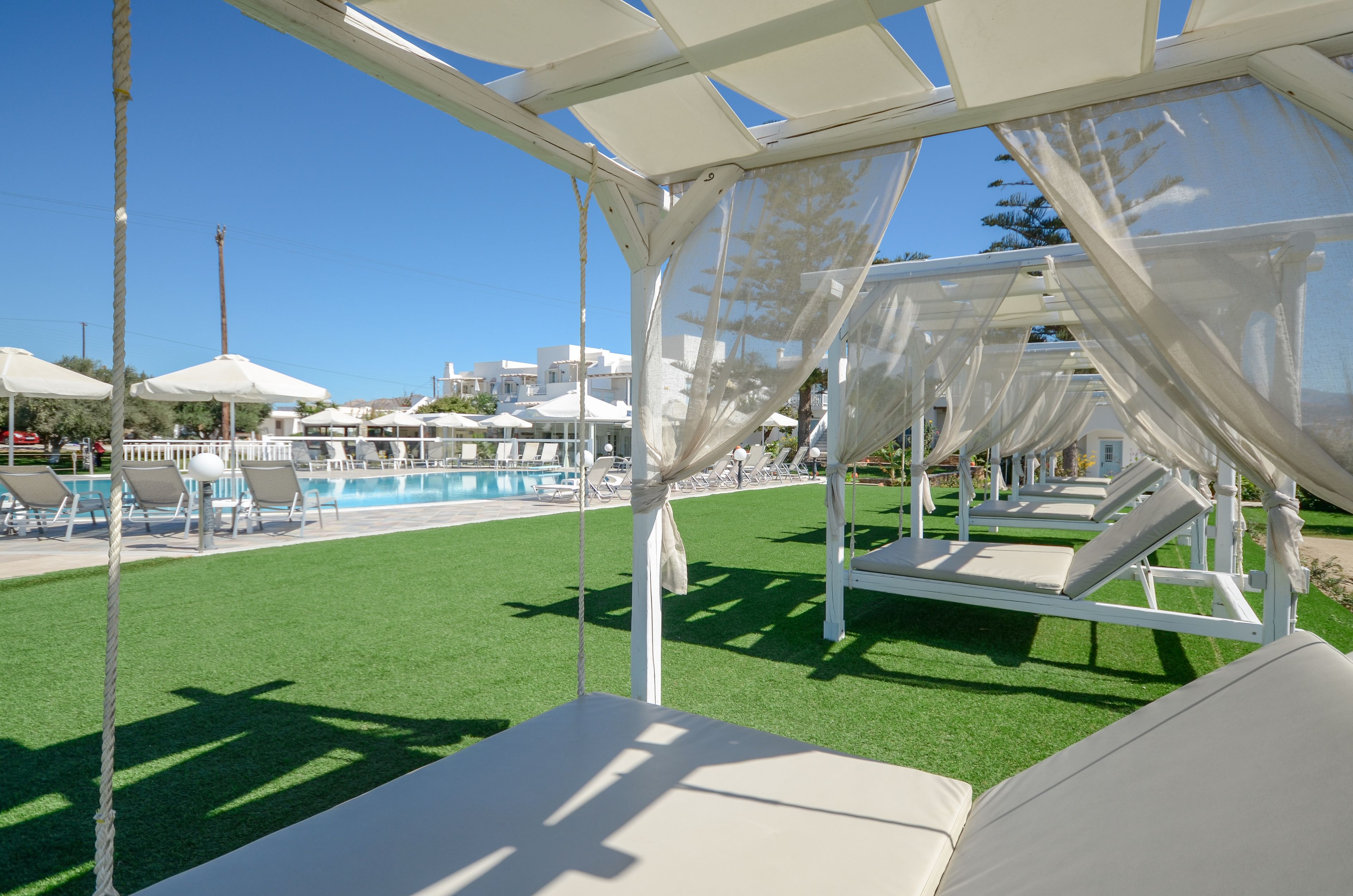Ein Poolbereich mit weißen Liegestühlen und Sonnenschirmen, einem wolkenlosen, blauen Himmel und einem Pool im Hintergrund.